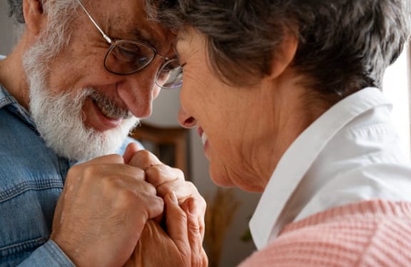 An elderly couple holding hands and resting their foreheads on each other